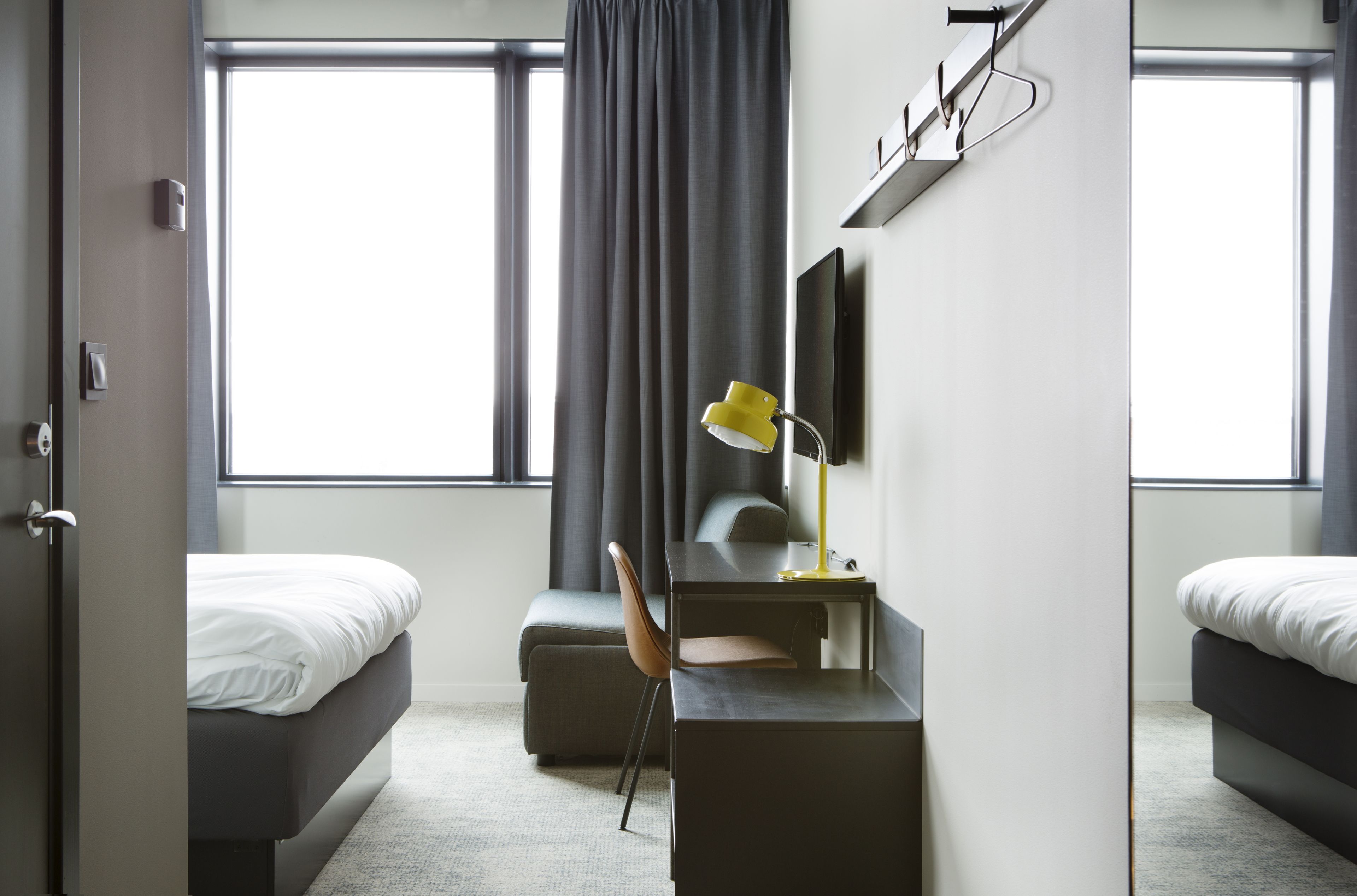 Una moderna camera d'hotel con un letto, una scrivania con una lampada e una grande finestra con tende.