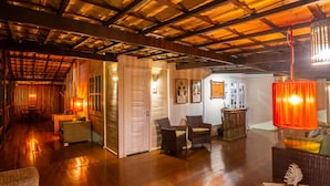 Un hall d’entrée spacieux doté d’un plancher en bois, d’un plafond haut avec des poutres apparentes, de meubles en osier et d’un éclairage chaleureux.