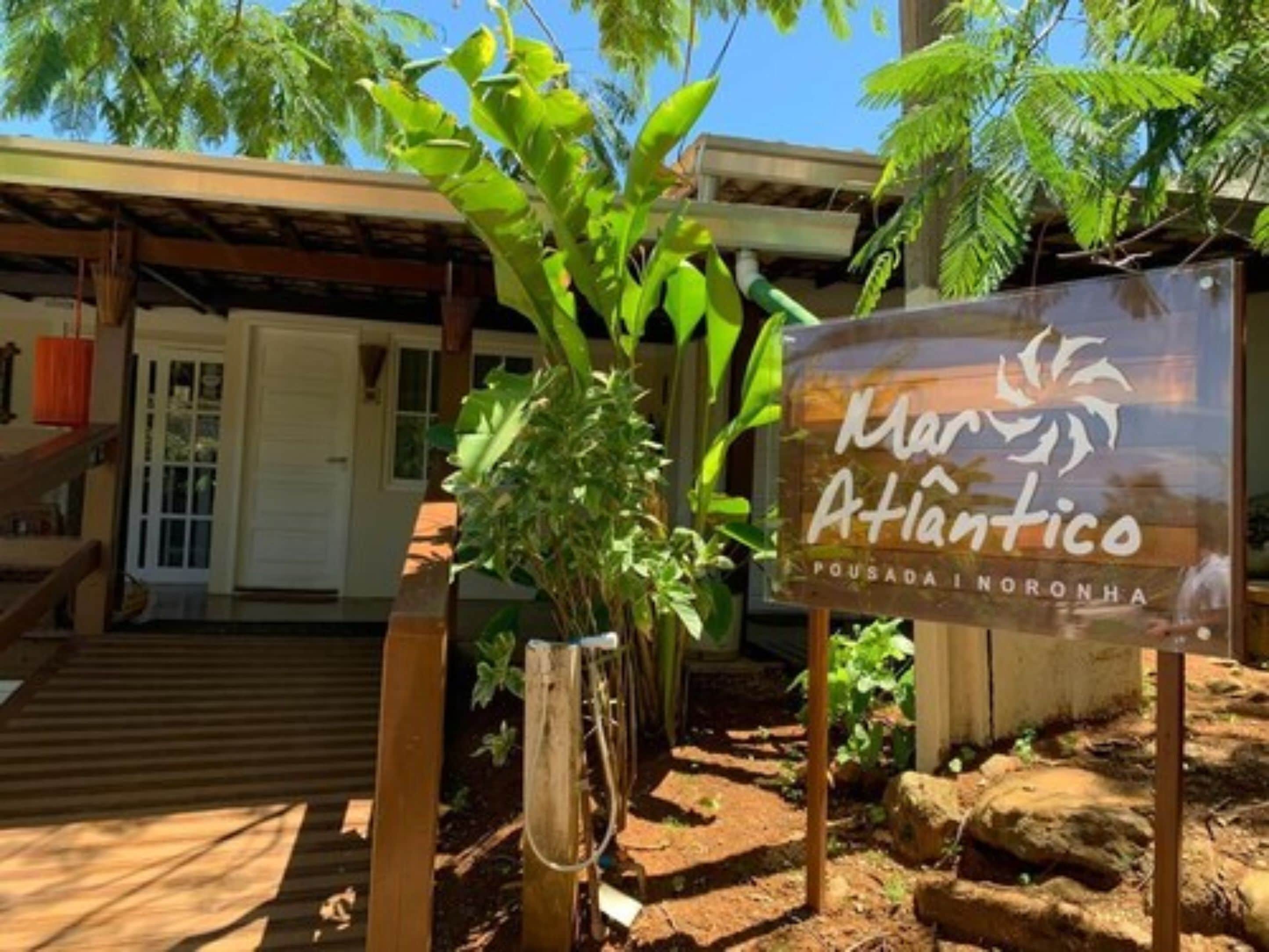 A sign for Mar Atlantico Pousada in a tropical setting with a wooden structure and lush greenery.