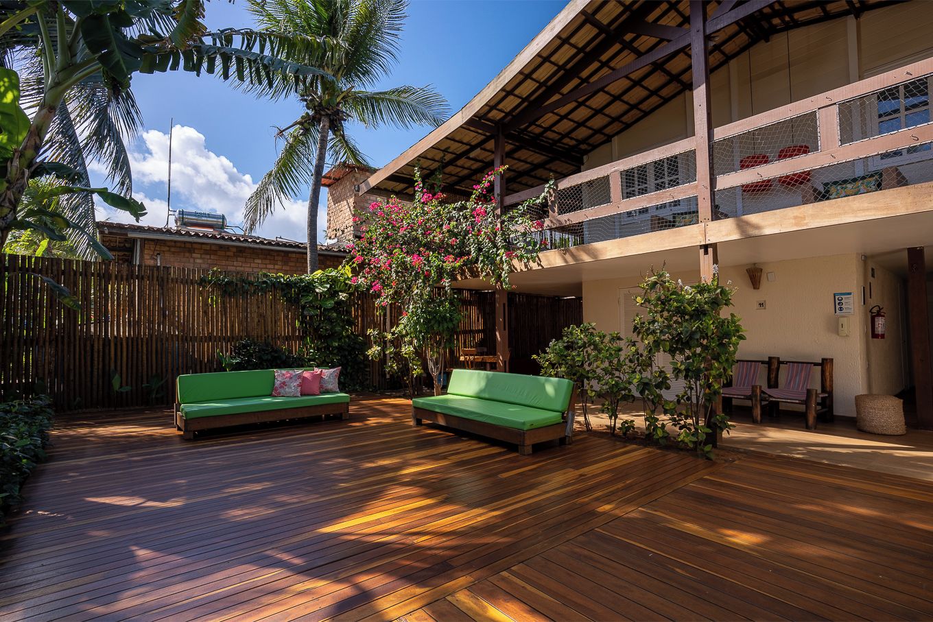 A wooden deck with two green sofas, a bamboo fence, and a balcony with a view of the sky.