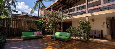 A wooden deck with two green sofas, a bamboo fence, and a balcony with a view of the sky.