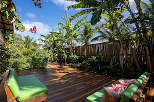A wooden deck with green cushioned seating, surrounded by lush tropical vegetation and a bamboo fence.