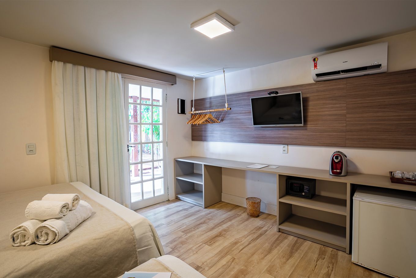 A hotel room with a bed, a desk, a TV, an air conditioner, and a window with curtains.