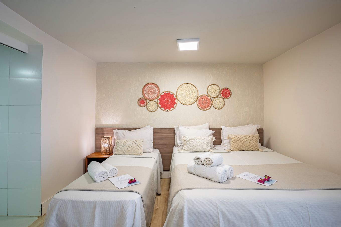 A hotel room with two beds, a wall decor with circular patterns, and a ceiling light.