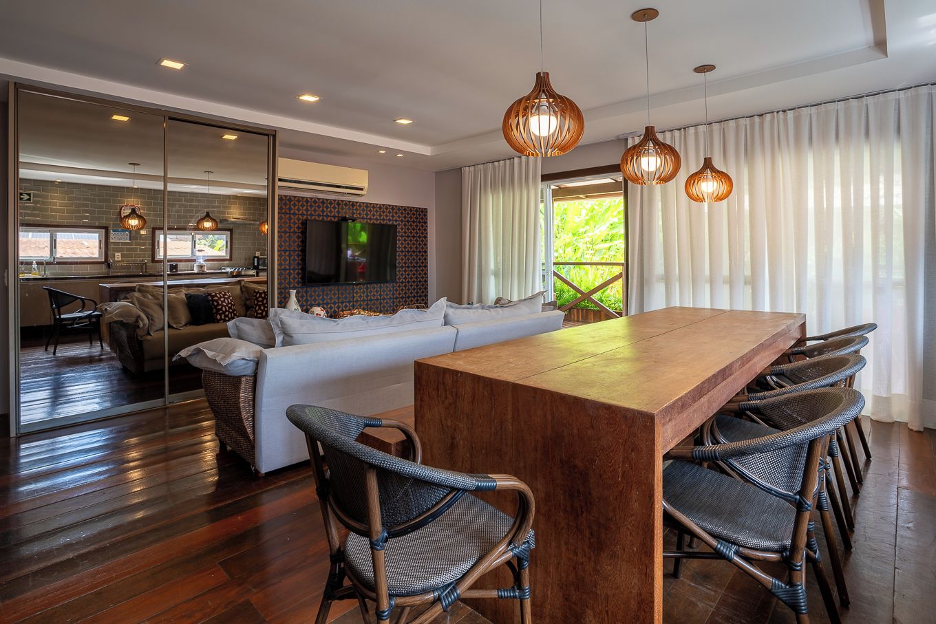 A modern kitchen with a large island, dining area with wicker chairs, and a living room with a sofa.