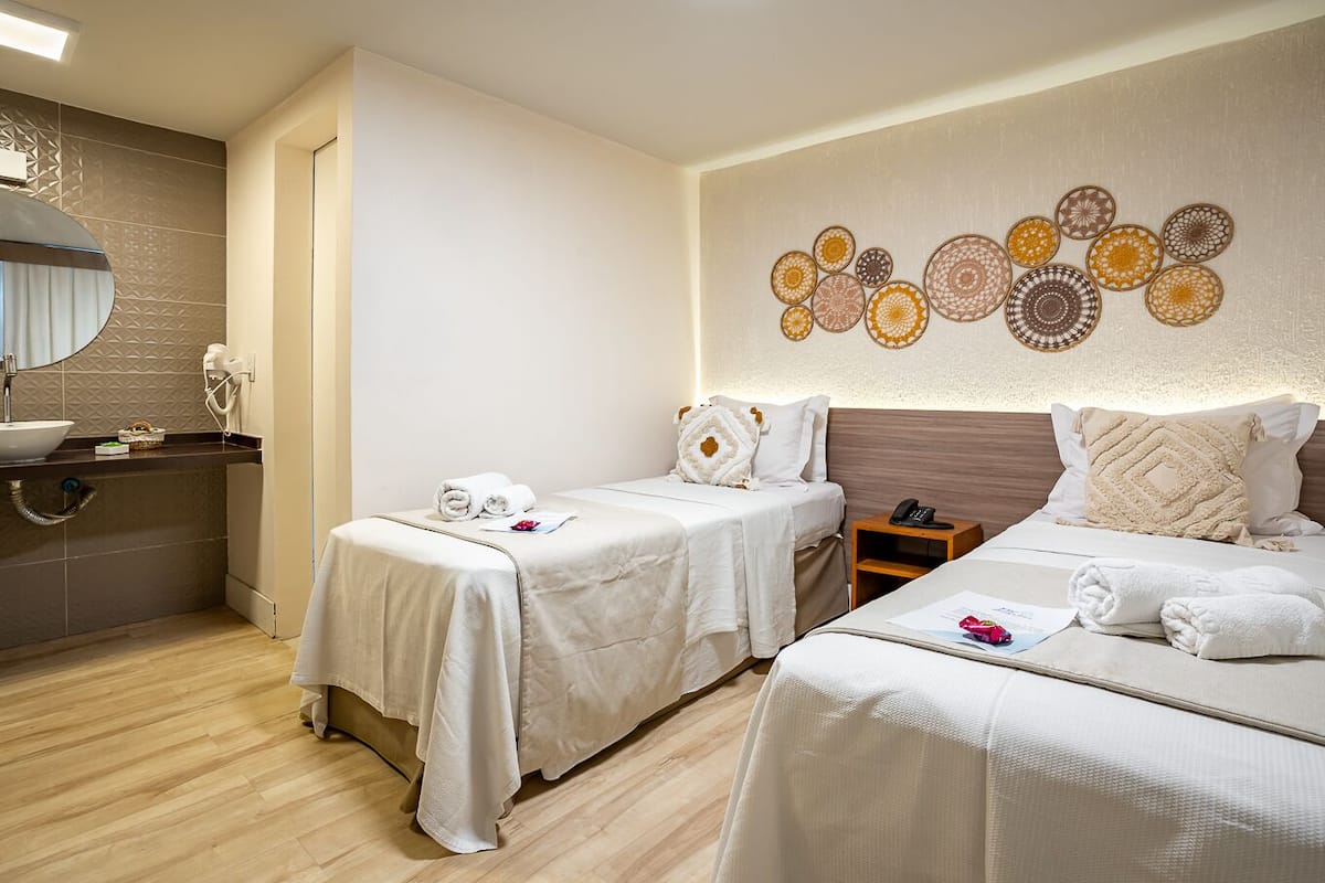 Ein Hotelzimmer mit zwei Betten, einem Badezimmer mit Waschbecken und einer Wand mit Dekoration.