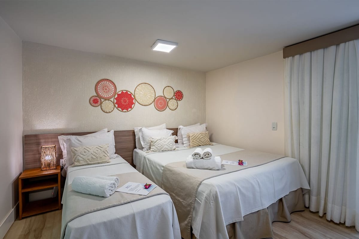 Ein Hotelzimmer mit zwei Betten, einem Nachttisch, Wanddekoration und einem Fenster mit Vorhängen.