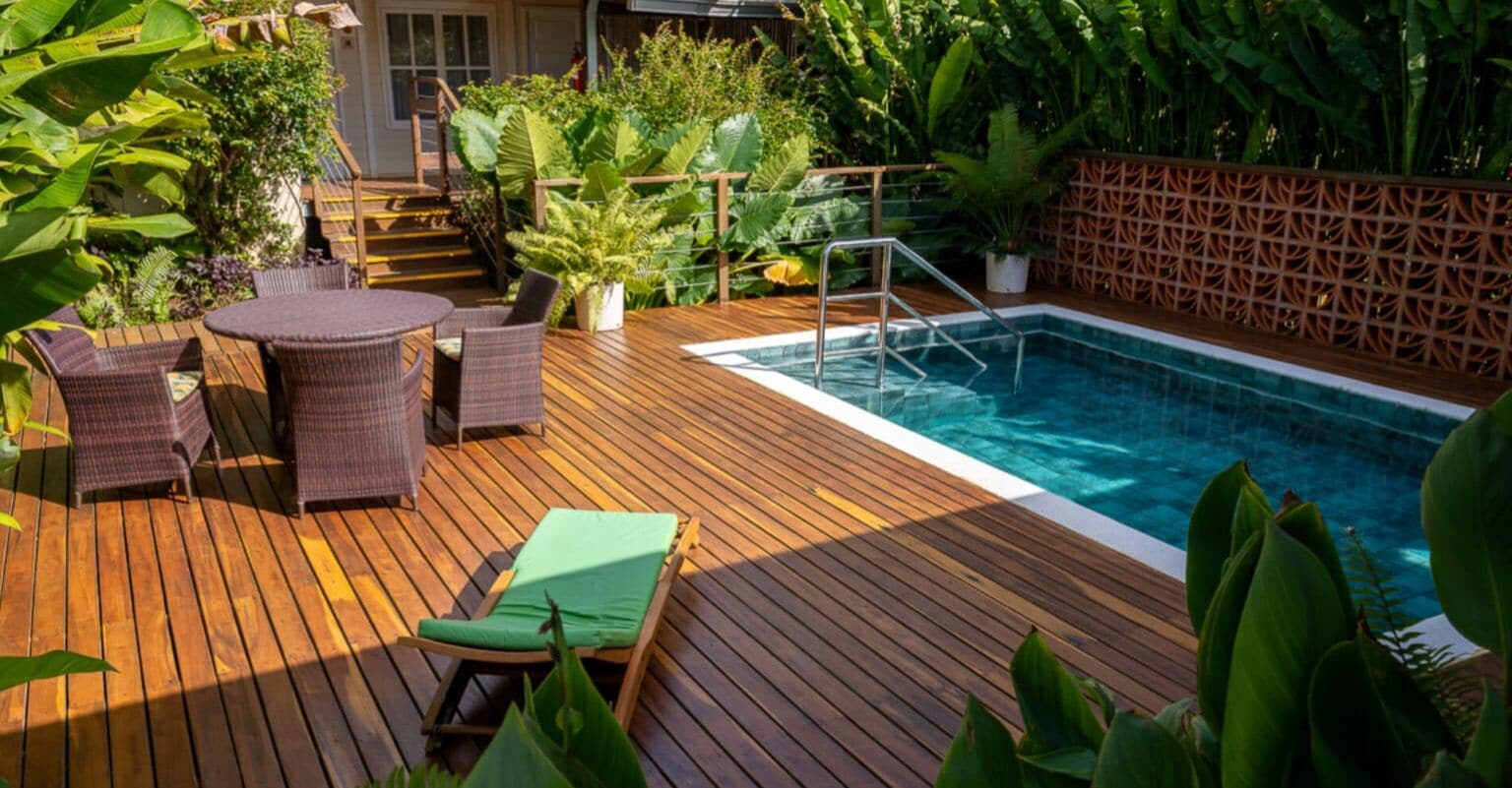 Terraza de madera con piscina, sillas de descanso y plantas en macetas.