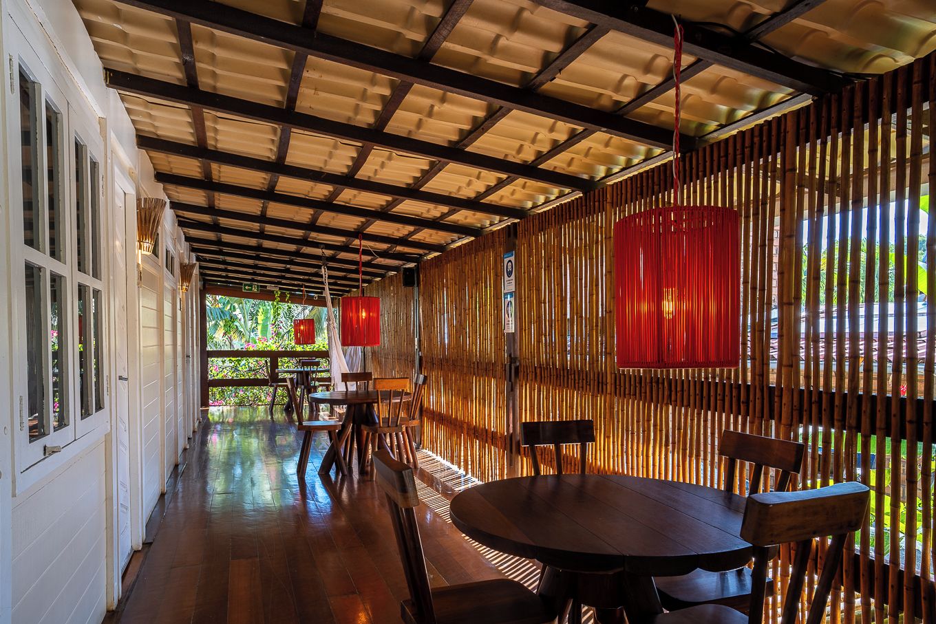 A covered outdoor area with wooden flooring, tables, chairs, and red lanterns.