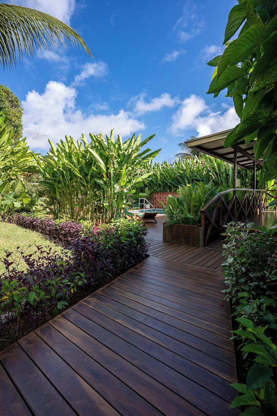 A wooden deck leading to a covered area with lush greenery and a clear blue sky.