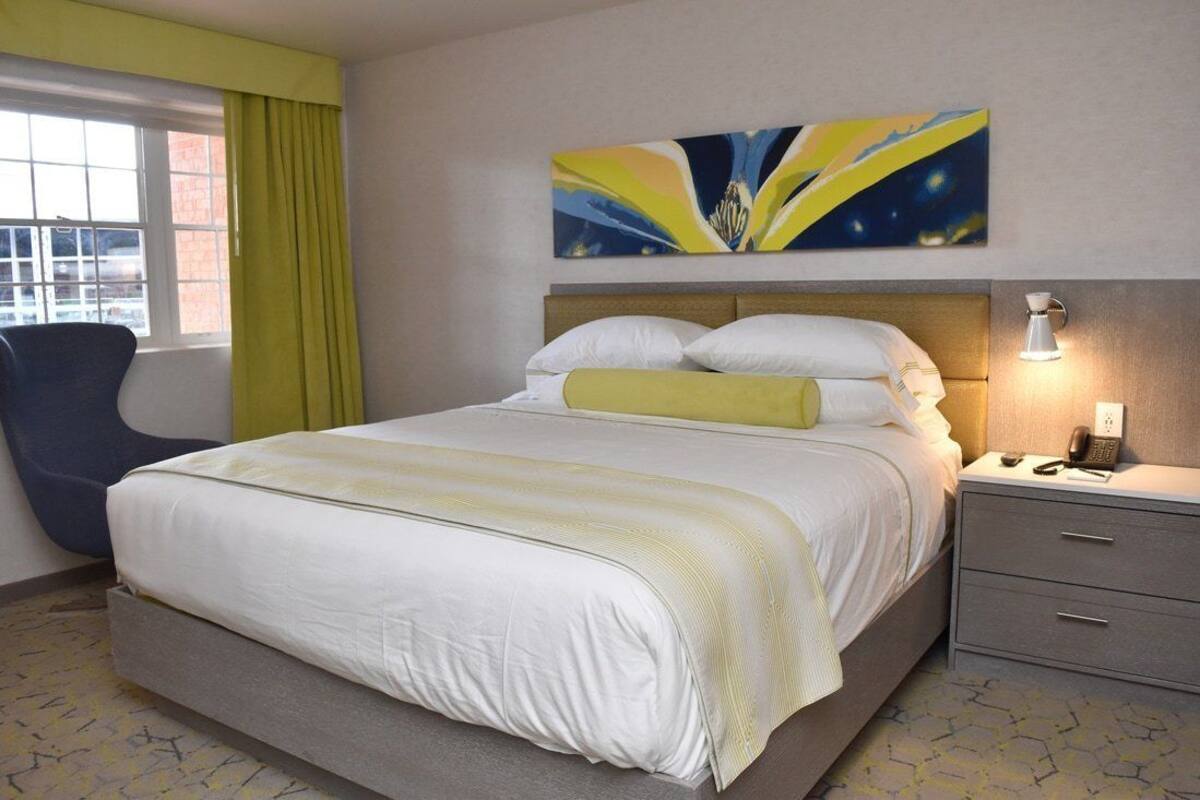 A hotel room with a large bed, a bedside table with a lamp, a chair, and a window with curtains.
