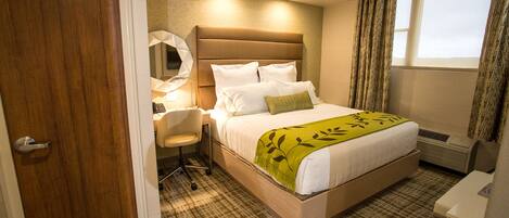 Ein Hotelzimmer mit Bett, Schreibtisch, Stuhl, Spiegel und einem Fenster mit Vorhängen.