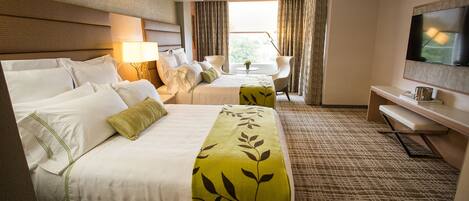 A hotel room with two beds, a TV, a desk, and a view of the outdoors.