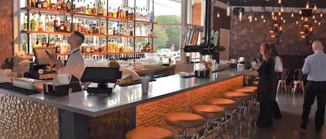 Een bar met een bartender, barstoelen, flessenkasten en een toonbank met een kassa.