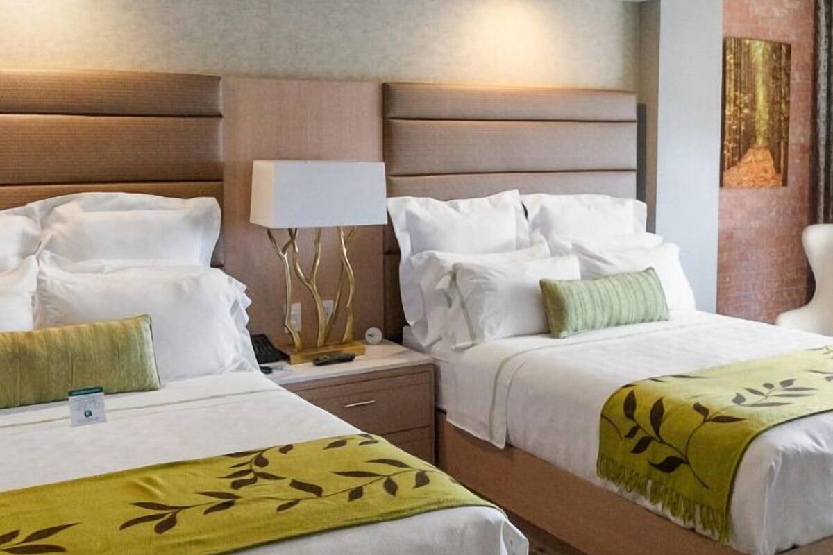 A hotel room with two beds, a nightstand, a lamp, and a painting on the wall.