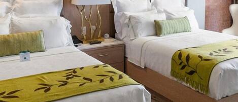 A hotel room with two beds, a nightstand, a lamp, and a painting on the wall.