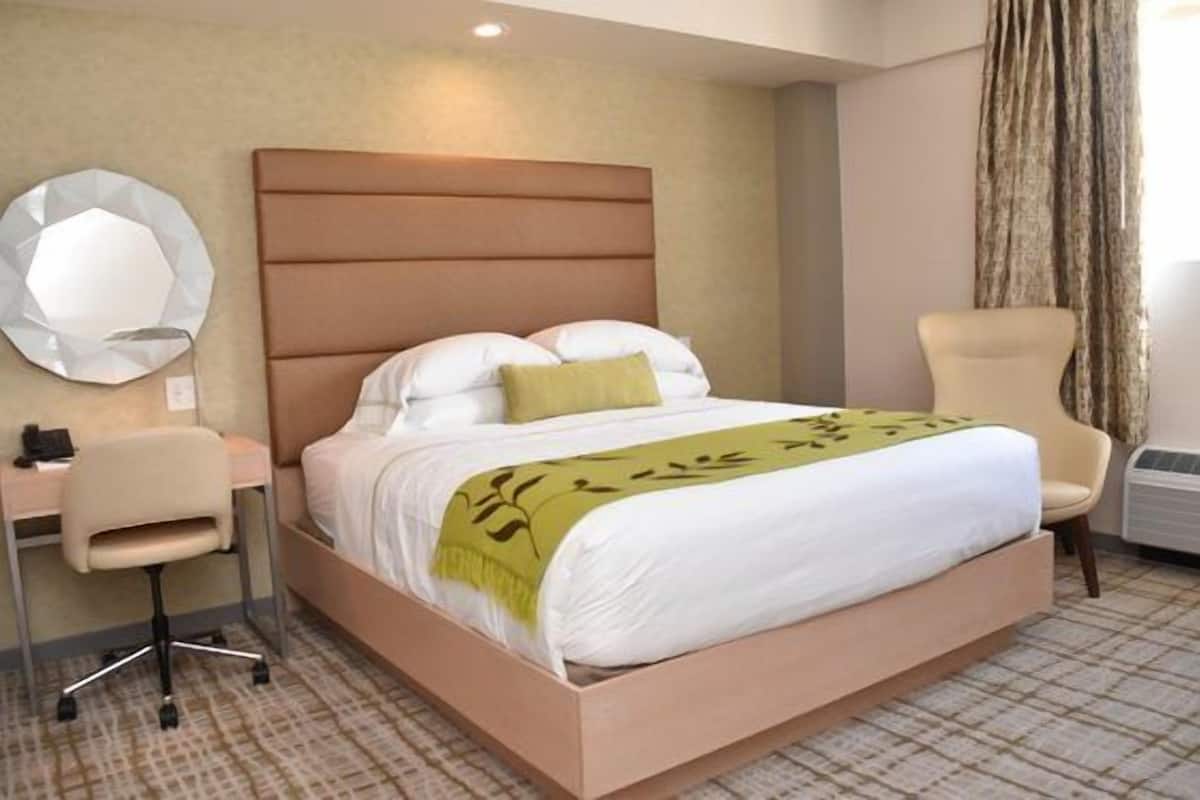 A hotel room with a bed, a desk, a chair, and a large mirror.