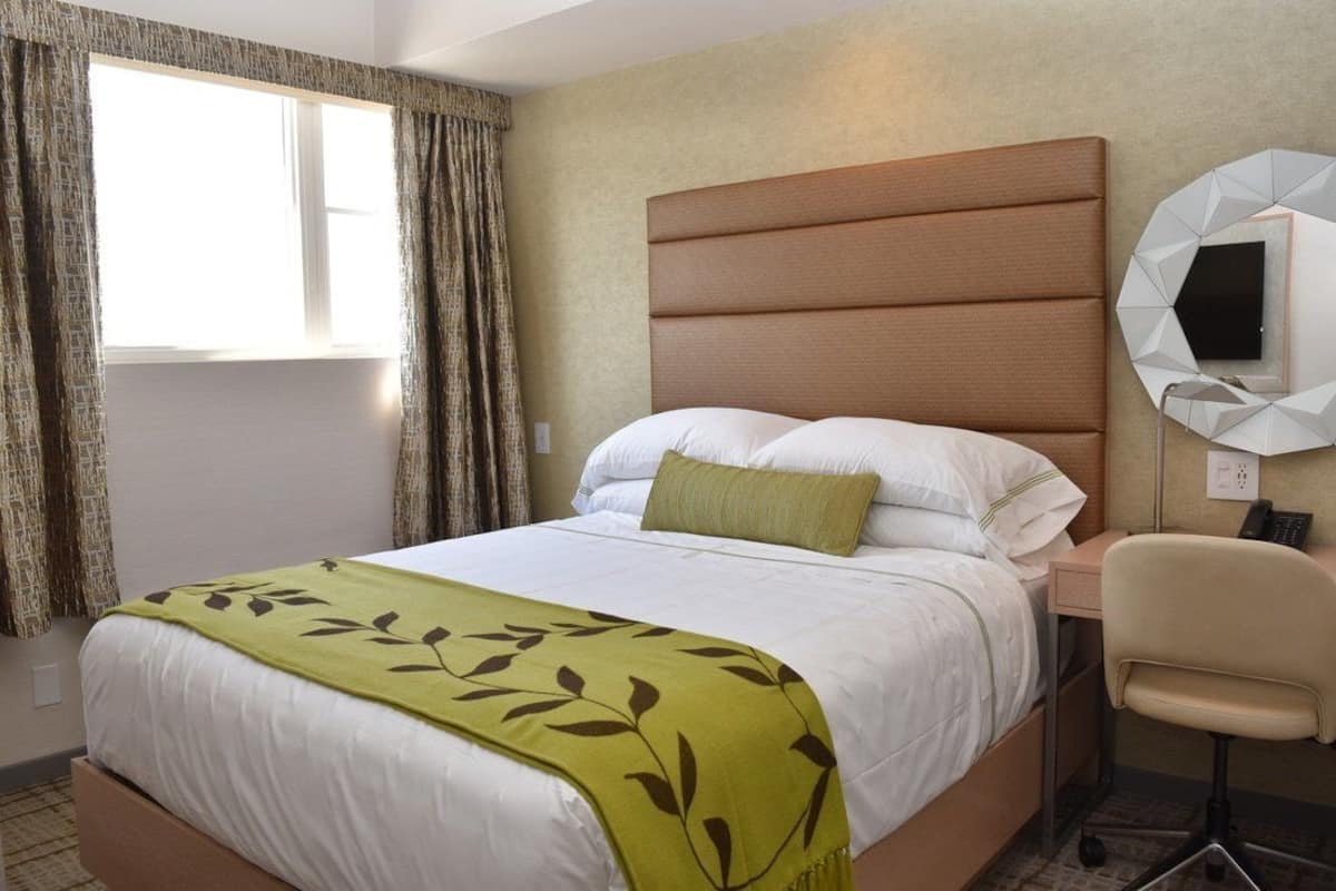 A hotel room with a bed, a desk, a chair, and a wall-mounted TV.