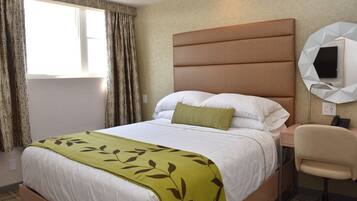 A hotel room with a bed, a desk, a chair, and a wall-mounted TV.