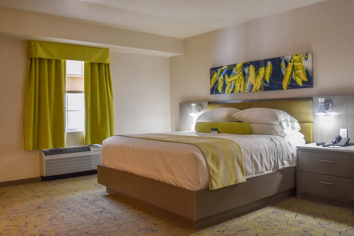 A hotel room with a bed, bedside tables, a painting, and a window with curtains.