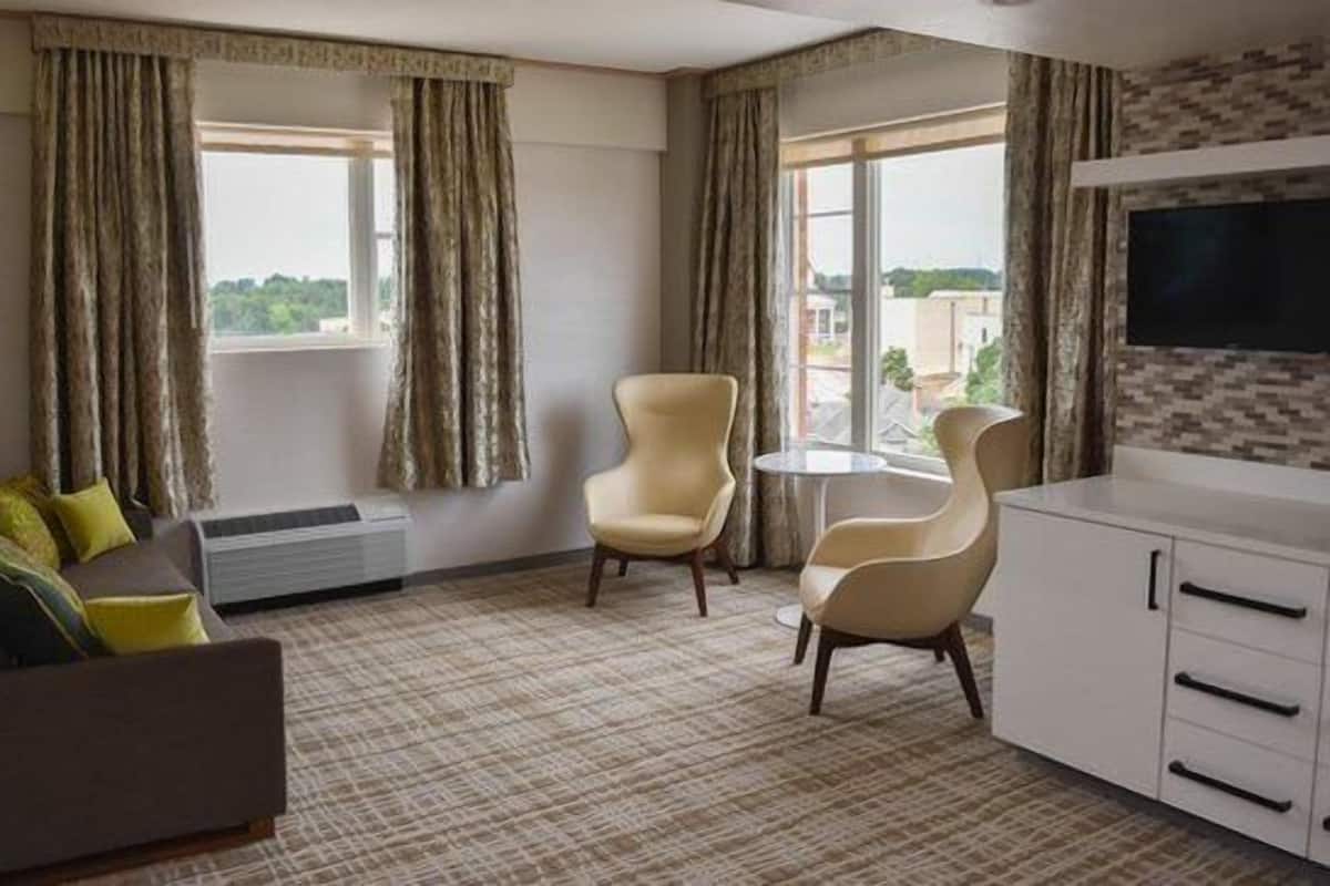 A hotel room with a sofa, two armchairs, a small table, a TV, and a window with curtains.