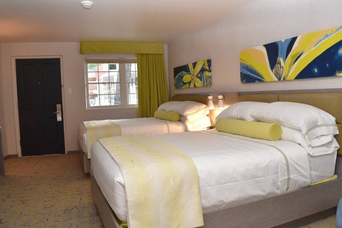 A hotel room with two beds, a window with curtains, and artwork on the wall.