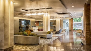Eine geräumige Lobby mit modernem Design, inklusive einer Rezeption, einer Sitzecke mit Sofas und einem großen Kunstwerk an der Wand.