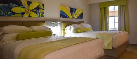 Habitación de hotel con dos camas, cada una con cabecero, un ventanal grande con cortinas y dos cuadros abstractos en la pared.