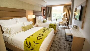 A hotel room with two beds, a desk, a chair, a TV, and a window with curtains.