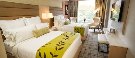 Ein Hotelzimmer mit zwei Betten, einem Schreibtisch, einem Stuhl, einem Fernseher und einem Fenster mit Vorhängen.