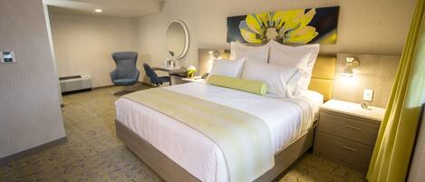 Habitación de hotel con una cama grande, un escritorio, una silla, un espejo y un cuadro de flores en la pared.