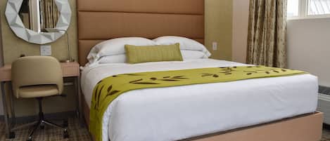 Une chambre d’hôtel avec un lit, un bureau et une chaise, un miroir rond et une fenêtre avec des rideaux.