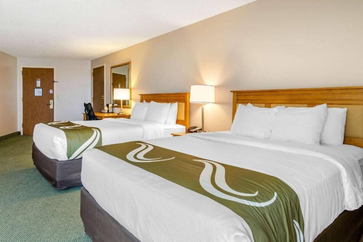 Ein Hotelzimmer mit zwei Betten, einem Schreibtisch, einem Stuhl, einem Spiegel und einer Lampe.