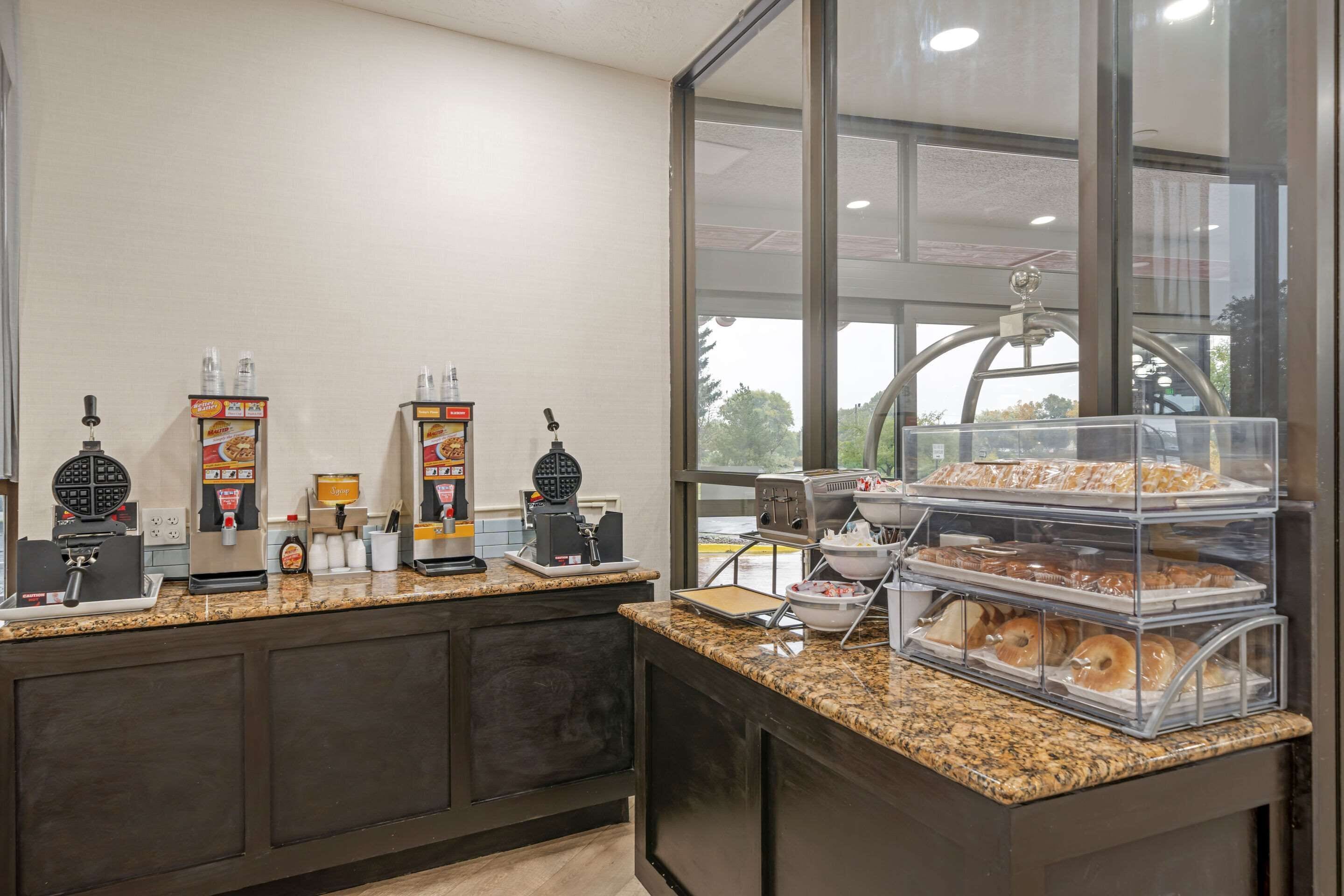 Una barra de desayuno con máquinas para hacer gofres, cafeteras y una vitrina con pasteles.