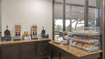A breakfast bar with waffle makers, coffee machines, and a display case with pastries.