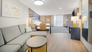 Una habitación de hotel moderna con sofá, una mesa redonda, un escritorio y un comedor con una silla.