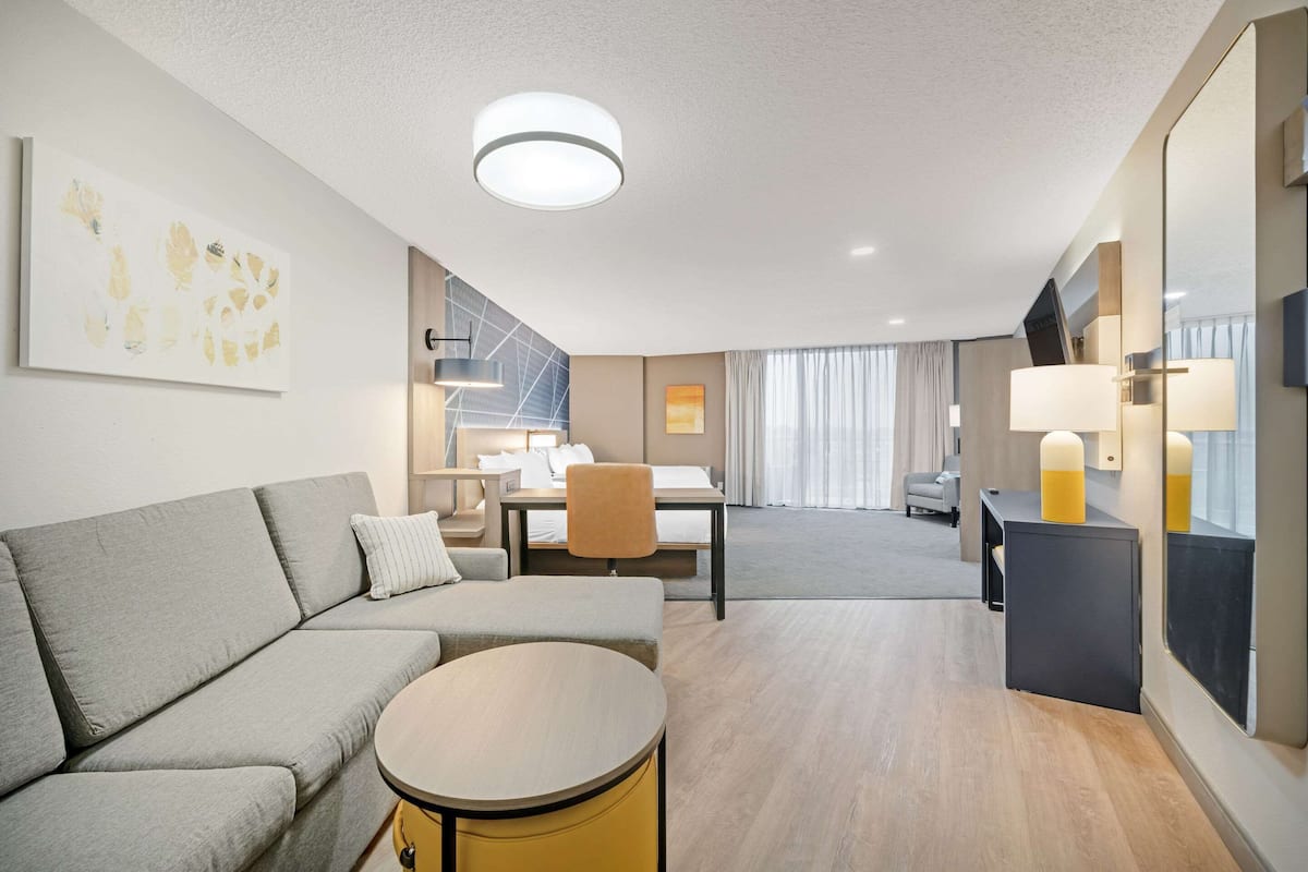 Ein modernes Hotelzimmer mit einer Couch, einem runden Tisch, einem Schreibtisch und einem Essbereich mit einem Stuhl.