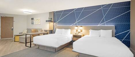 A hotel room with two beds, a desk, and a chair. There are wall-mounted lamps and a door.