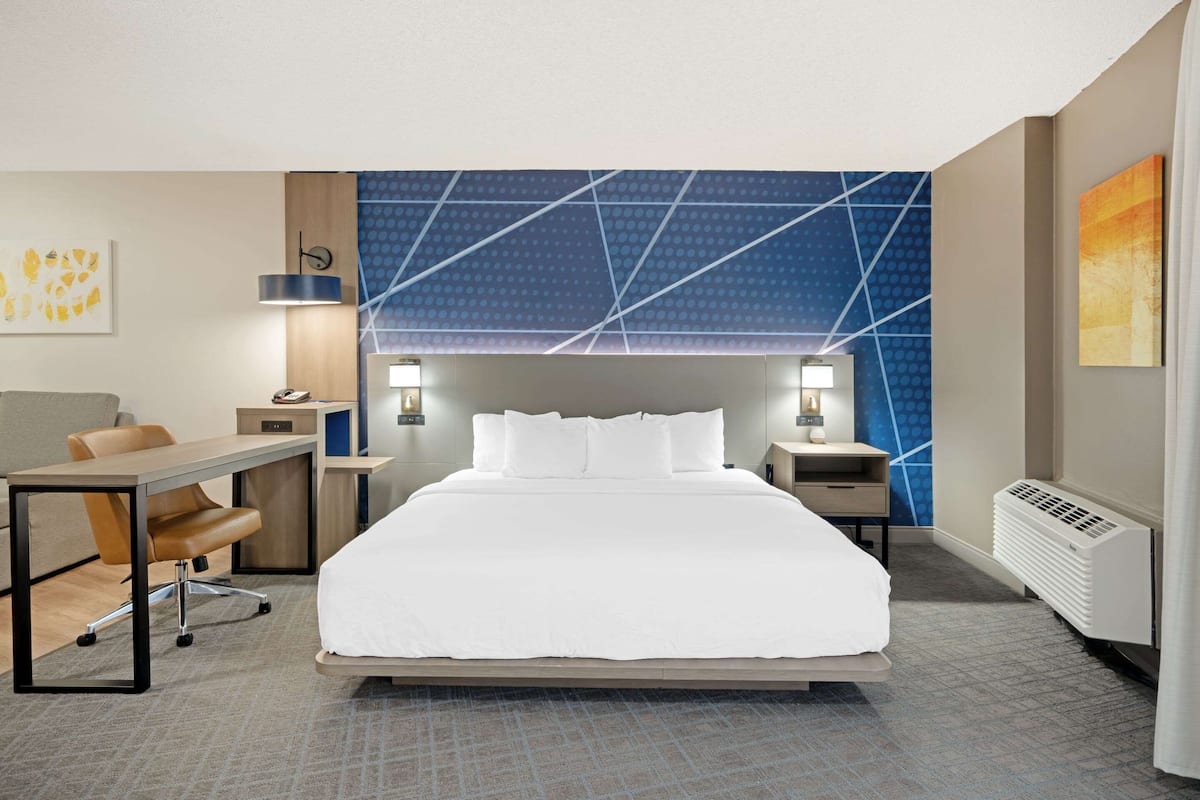 Ein Hotelzimmer mit einem großen Bett, einem Schreibtisch, zwei Stühlen, einem Nachttisch und einer Wand mit geometrischem Muster.