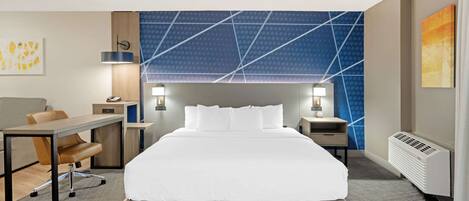 A hotel room with a large bed, a desk, two chairs, a nightstand, and a wall with a geometric pattern.