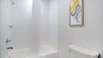 A bathroom with a white bathtub, a showerhead, a toilet, and a framed abstract painting on the wall.