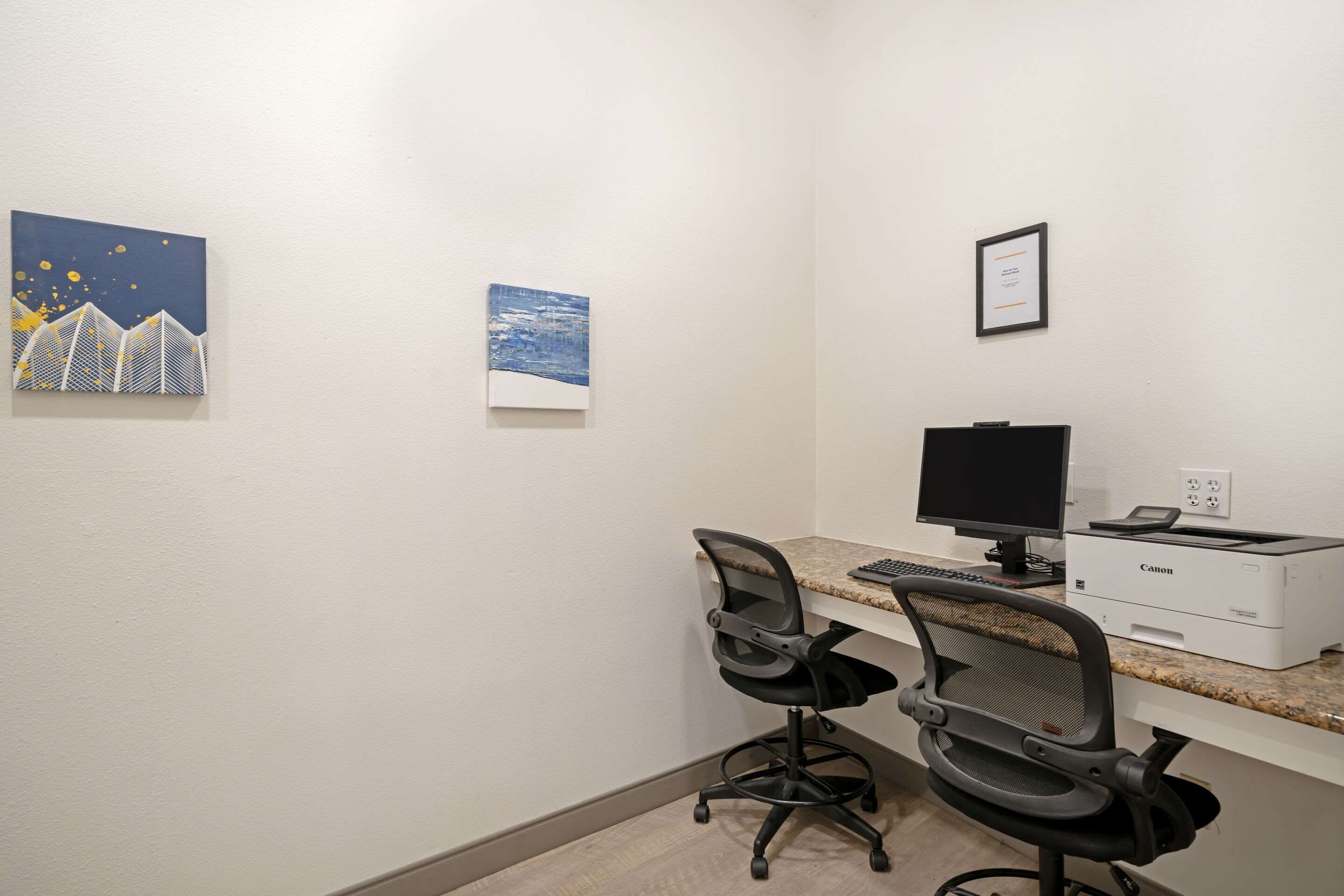 A workspace with two office chairs, a computer monitor, and a printer on a counter.