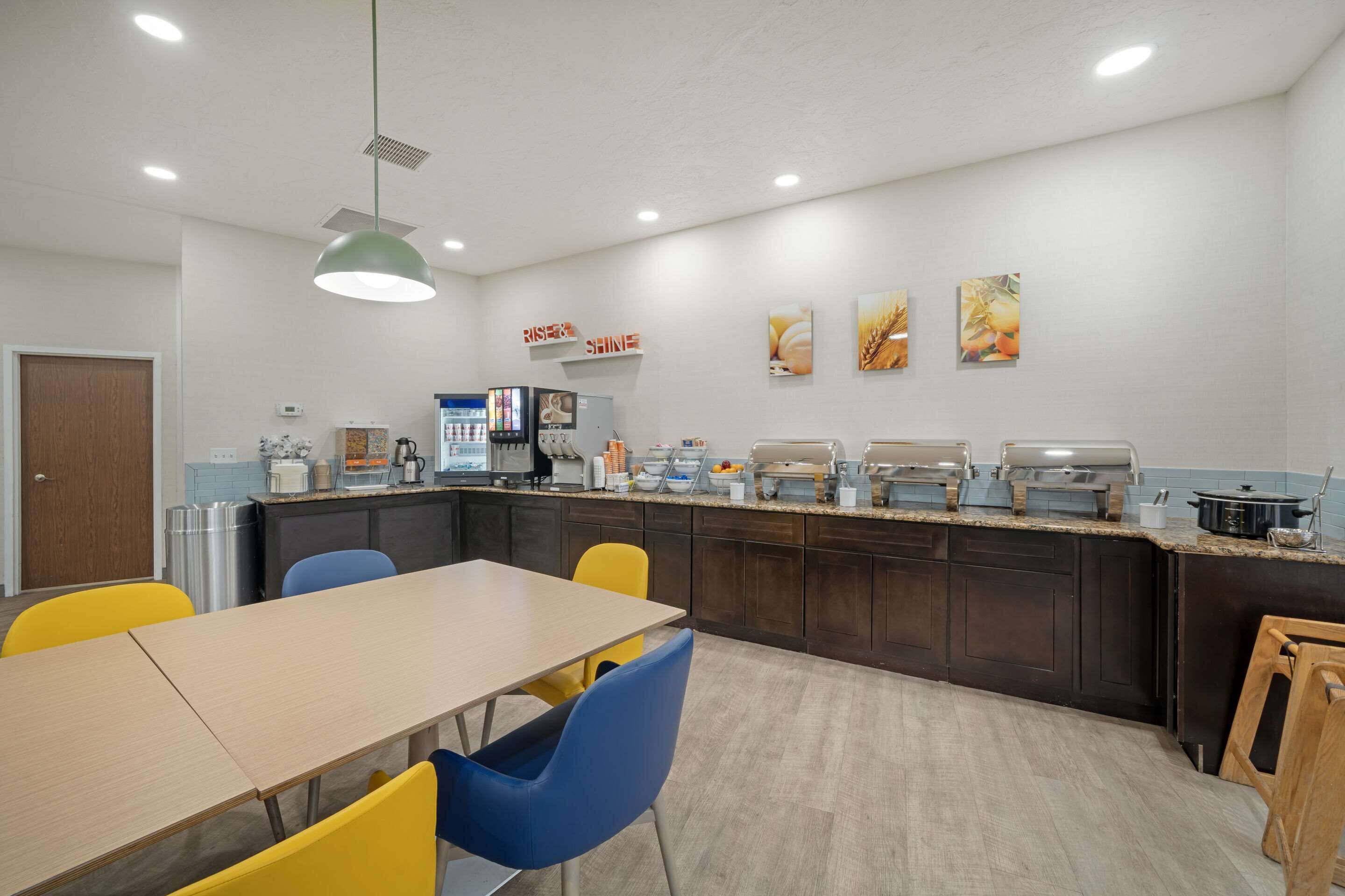 A modern kitchen with a long counter, yellow chairs, and a wooden table.