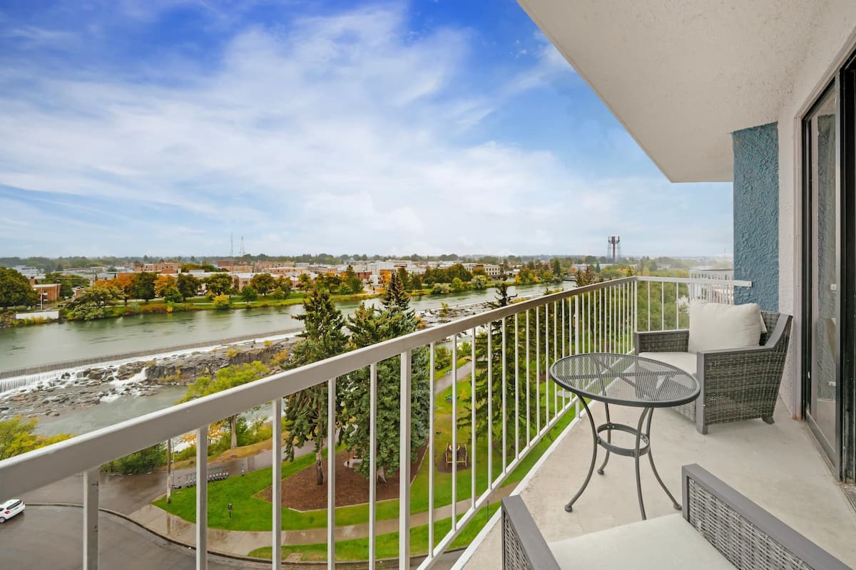 Ein Balkon mit Blick auf einen Fluss, Grünflächen und entfernte Gebäude.