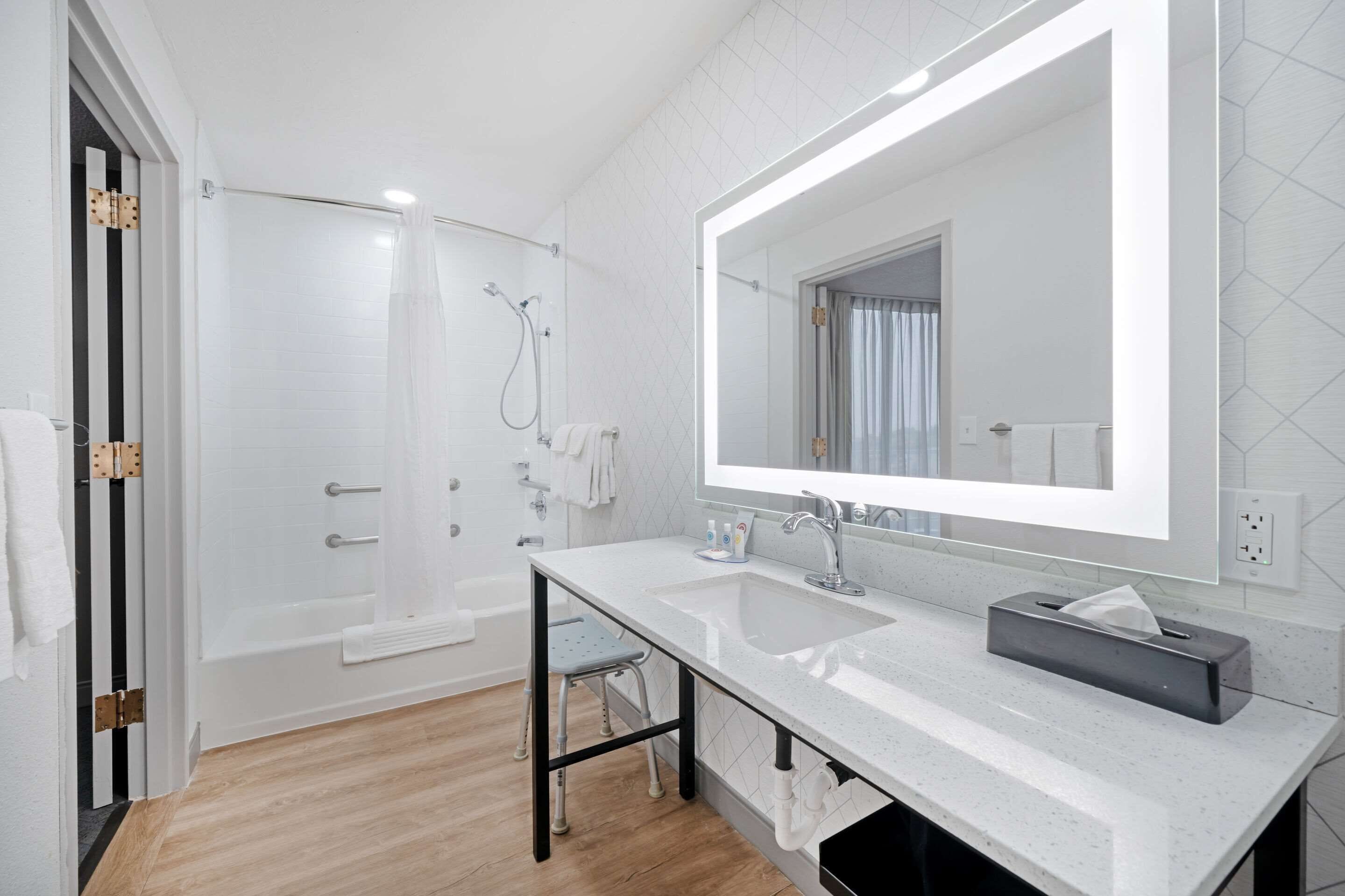 A modern bathroom with a large mirror, a bathtub, a shower, and a sink.