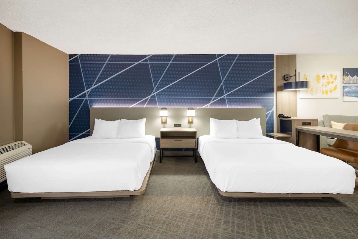 Ein Hotelzimmer mit zwei Betten, einem Schreibtisch, einem Sessel und einem Nachttisch mit Lampen.