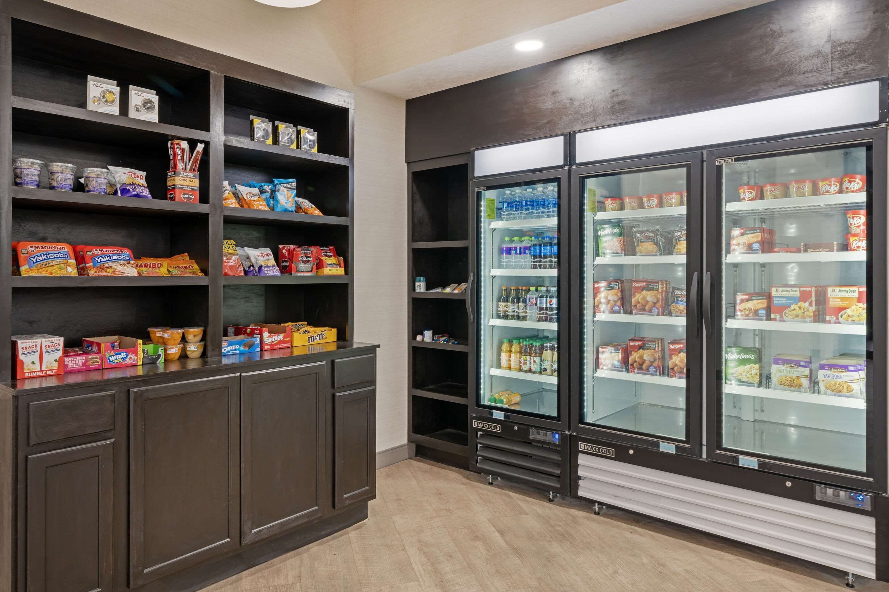A snack bar with shelves stocked with various snacks and a refrigerator with beverages.