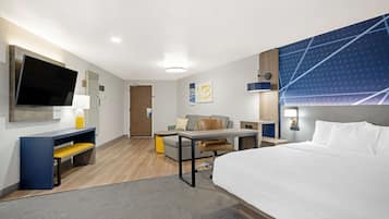 A modern hotel room with a large bed, a desk with a chair, a sofa, and a TV.