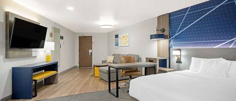 A modern hotel room with a large bed, a desk with a chair, a sofa, and a TV.