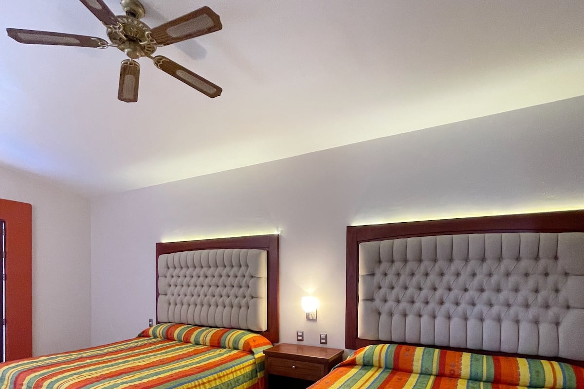 A hotel room with two beds, a ceiling fan, and a nightstand with a lamp.